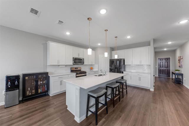 kitchen featuring visible vents, dark wood finished floors, a center island with sink, a breakfast bar, and stainless steel appliances