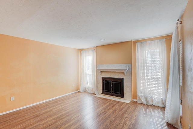 unfurnished living room featuring a textured ceiling, a premium fireplace, baseboards, and wood finished floors