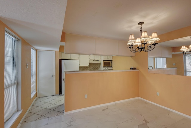 kitchen with a chandelier, marble finish floor, light countertops, stainless steel microwave, and decorative light fixtures