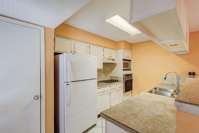 kitchen with tile countertops, stainless steel microwave, wall oven, freestanding refrigerator, and a sink