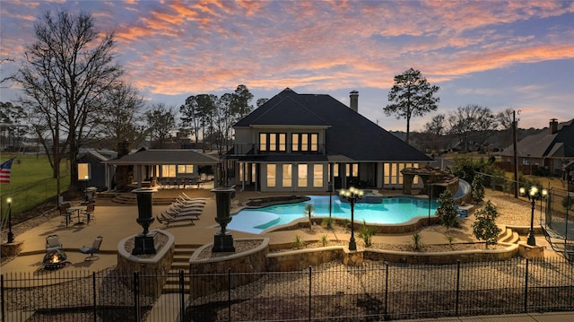 back house at dusk with a fenced in pool, a fire pit, a patio area, and a gazebo