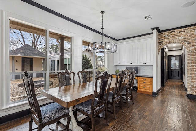 dining area with crown molding, brick wall, an inviting chandelier, and dark hardwood / wood-style flooring