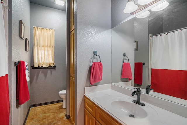 full bathroom featuring a textured wall, vanity, and toilet