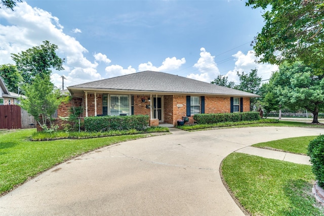 ranch-style house featuring brick siding, a shingled roof, concrete driveway, a front yard, and fence