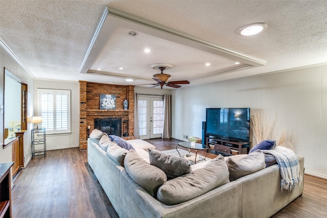 living area with ornamental molding, wood finished floors, a tray ceiling, a textured ceiling, and french doors