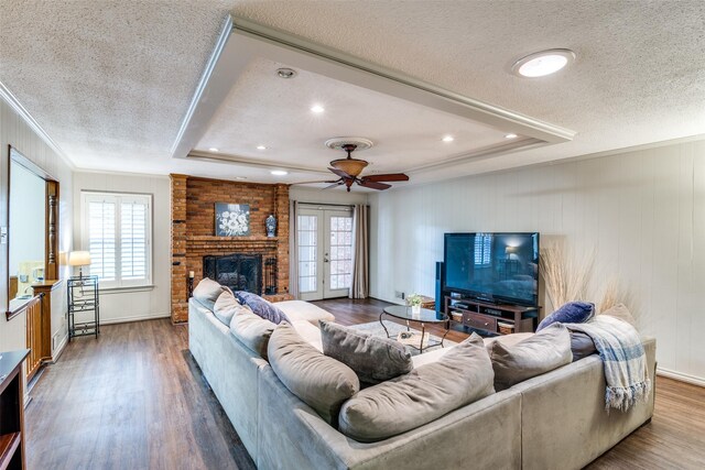 living area with a tray ceiling, plenty of natural light, wood finished floors, and french doors