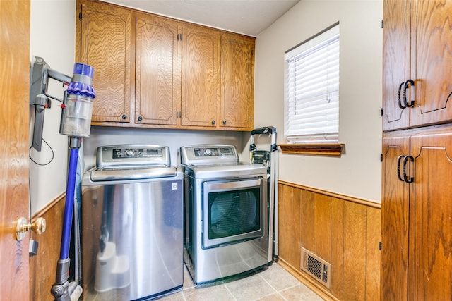 washroom with light tile patterned floors, wooden walls, cabinets, and washing machine and clothes dryer