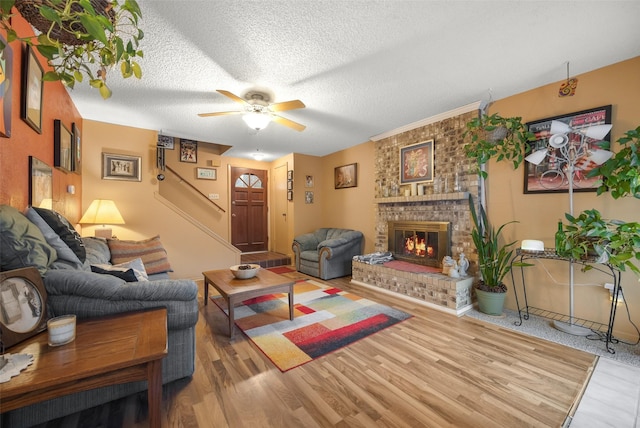 living room featuring hardwood / wood-style flooring, ceiling fan, a brick fireplace, and a textured ceiling