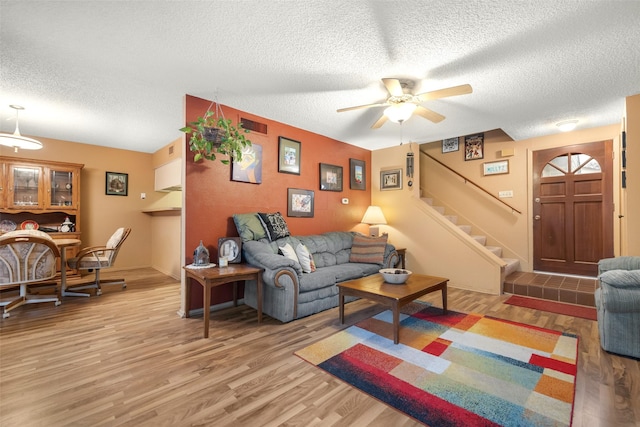 living room featuring ceiling fan, a textured ceiling, and light wood-type flooring