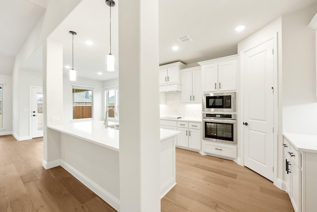 kitchen featuring white cabinetry, built in microwave, decorative light fixtures, and stainless steel oven