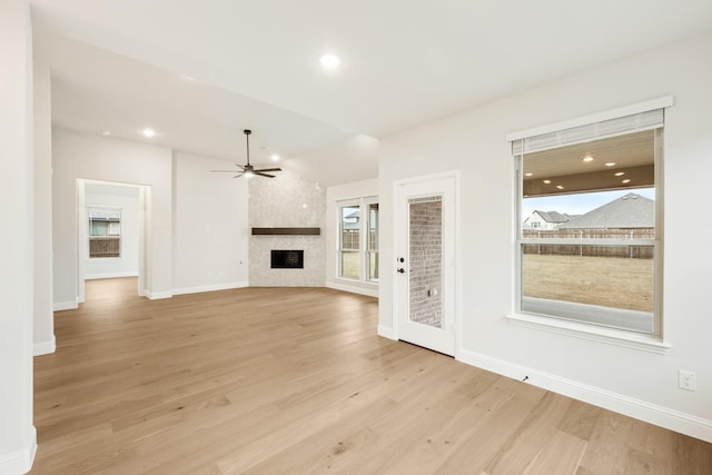 unfurnished living room with lofted ceiling, light hardwood / wood-style floors, a large fireplace, and ceiling fan