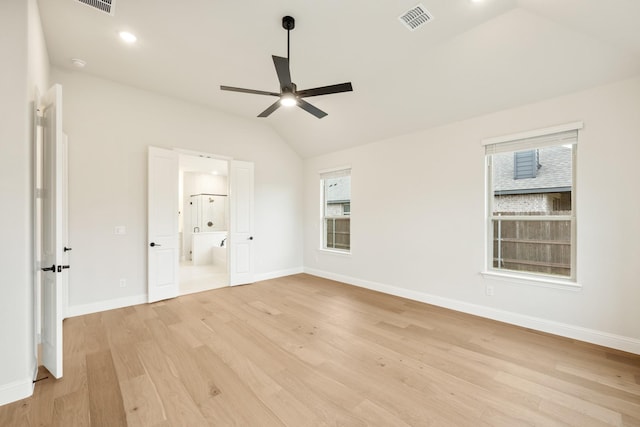 unfurnished bedroom featuring multiple windows, vaulted ceiling, connected bathroom, and light hardwood / wood-style floors