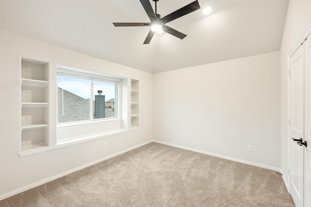 empty room featuring light carpet, built in shelves, vaulted ceiling, and ceiling fan