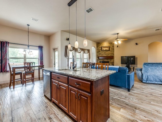 kitchen featuring light stone counters, decorative light fixtures, an island with sink, and dishwasher