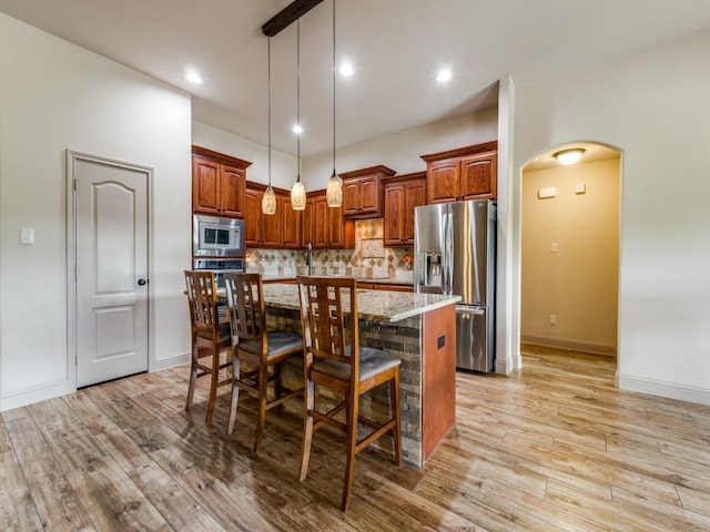 kitchen with a breakfast bar, appliances with stainless steel finishes, a kitchen island with sink, light stone countertops, and decorative light fixtures