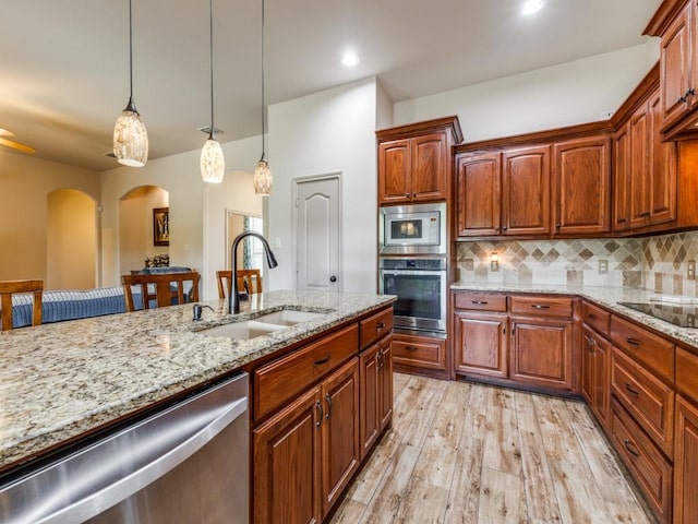 kitchen featuring sink, hanging light fixtures, light wood-type flooring, appliances with stainless steel finishes, and backsplash