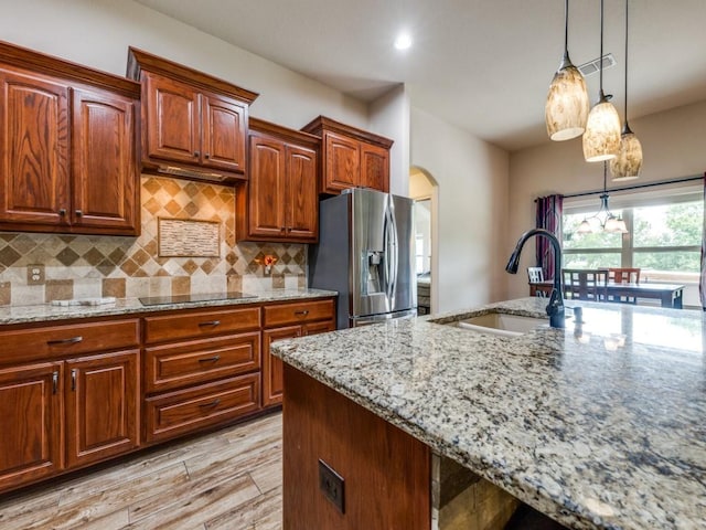 kitchen with sink, hanging light fixtures, black electric stovetop, stainless steel fridge with ice dispenser, and light stone countertops