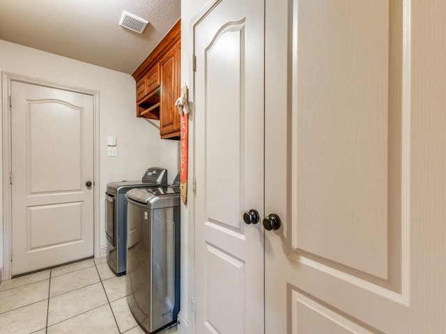 washroom featuring separate washer and dryer, light tile patterned floors, cabinets, and a textured ceiling