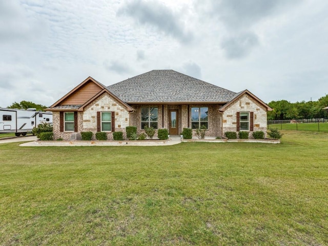 view of front of house with a front yard, fence, stone siding, and a shingled roof