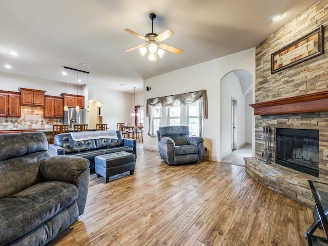 living room featuring ceiling fan, a fireplace, and light wood-type flooring