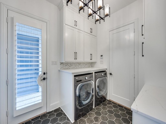 clothes washing area featuring a notable chandelier, cabinets, washing machine and dryer, and a wealth of natural light