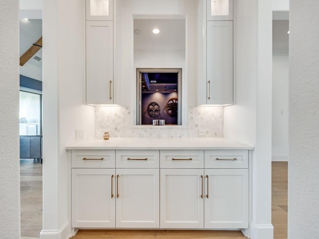 bar featuring backsplash, light hardwood / wood-style floors, and white cabinets