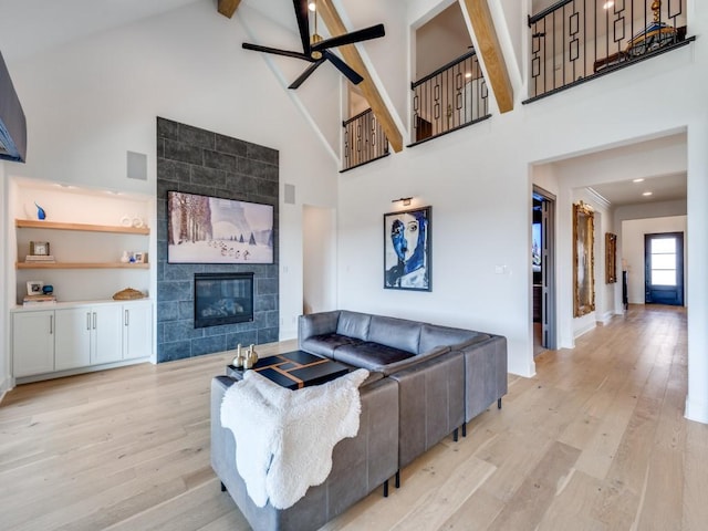 living room featuring ceiling fan, beam ceiling, high vaulted ceiling, a fireplace, and light hardwood / wood-style floors