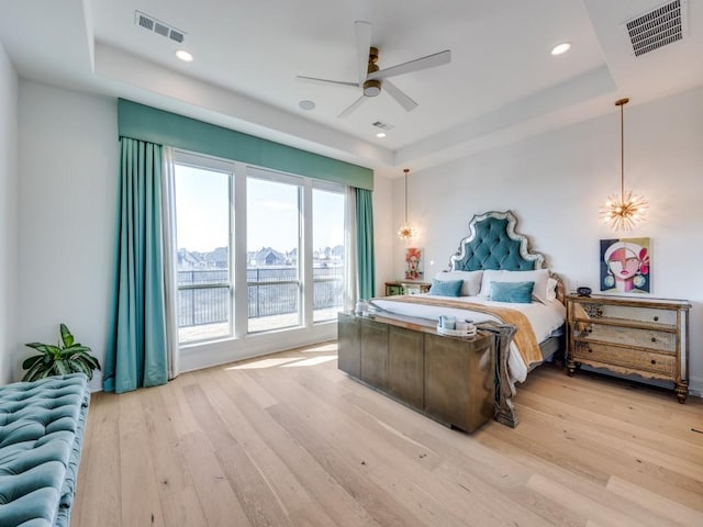 bedroom with ceiling fan, a tray ceiling, and light hardwood / wood-style floors