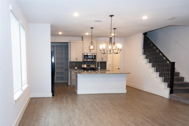 kitchen featuring stone counters, appliances with stainless steel finishes, decorative light fixtures, a kitchen island with sink, and light hardwood / wood-style flooring