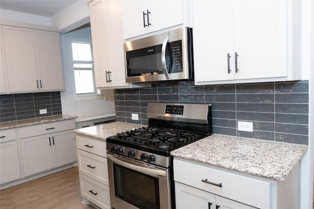 kitchen featuring appliances with stainless steel finishes, tasteful backsplash, white cabinets, light stone counters, and light wood-type flooring