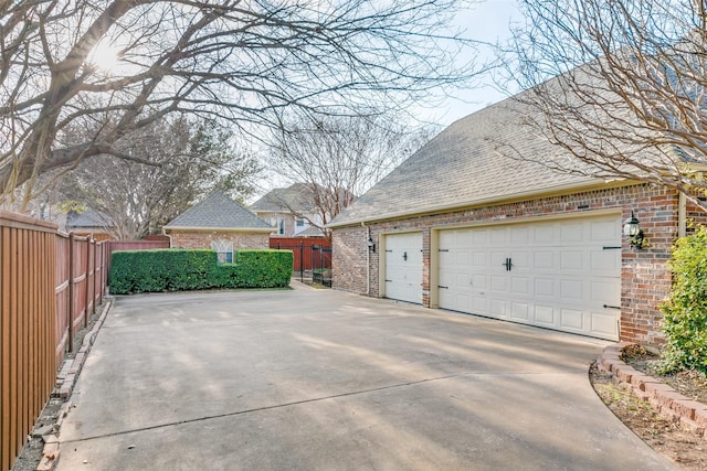 view of side of property featuring a garage, brick siding, a shingled roof, and fence