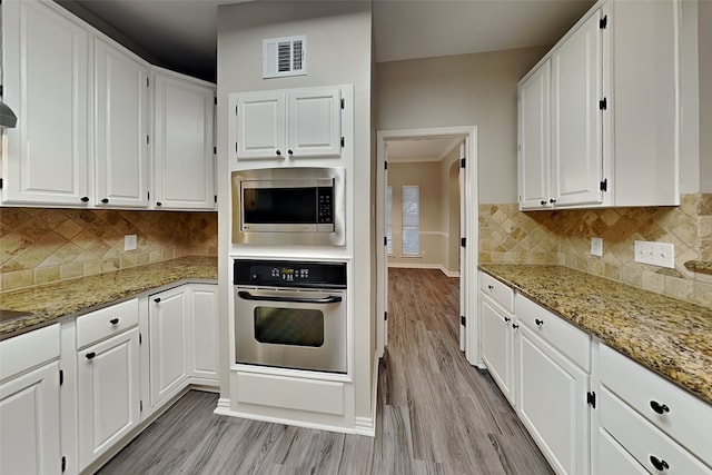 kitchen with stainless steel appliances, white cabinetry, and light stone countertops