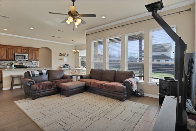 living room with ceiling fan, ornamental molding, light hardwood / wood-style floors, and a wood stove