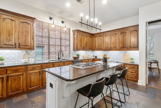 kitchen with pendant lighting, sink, a breakfast bar area, dark stone countertops, and a kitchen island