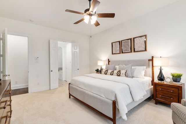 bedroom with ceiling fan, light colored carpet, and connected bathroom