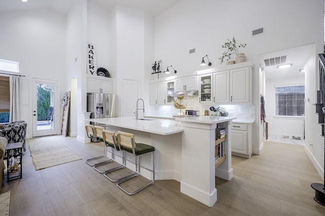 kitchen with sink, stainless steel fridge, white cabinets, a kitchen bar, and a kitchen island with sink