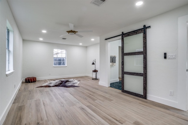 spare room with ceiling fan, a barn door, and light hardwood / wood-style flooring