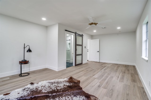 unfurnished bedroom with ceiling fan, a barn door, ensuite bath, and light wood-type flooring