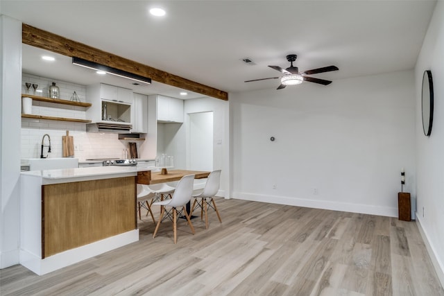 kitchen with sink, white cabinetry, light hardwood / wood-style flooring, beam ceiling, and decorative backsplash