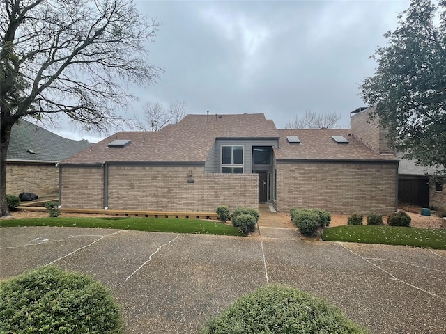 exterior space with a shingled roof, a chimney, and brick siding