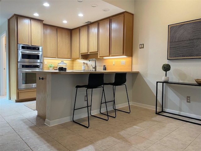 kitchen featuring visible vents, a breakfast bar, a peninsula, stainless steel double oven, and backsplash