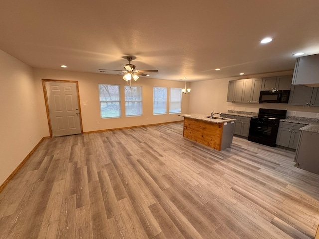 kitchen featuring gray cabinetry, light hardwood / wood-style flooring, an island with sink, pendant lighting, and black appliances