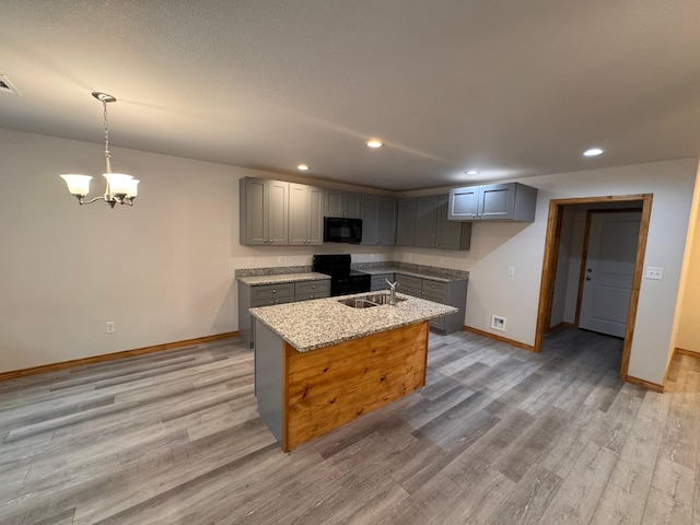 kitchen featuring sink, gray cabinetry, light stone counters, black appliances, and an island with sink