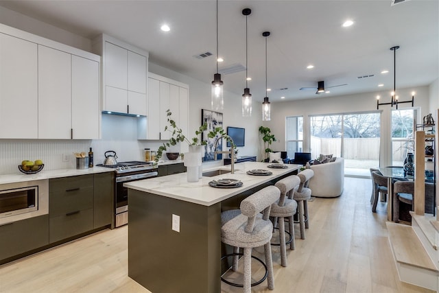 417 Wayne St, Dallas, TX 75223 - kitchen featuring a kitchen island with sink, modern cabinets, light wood-style floors, a breakfast bar area, and appliances with stainless steel finishes
