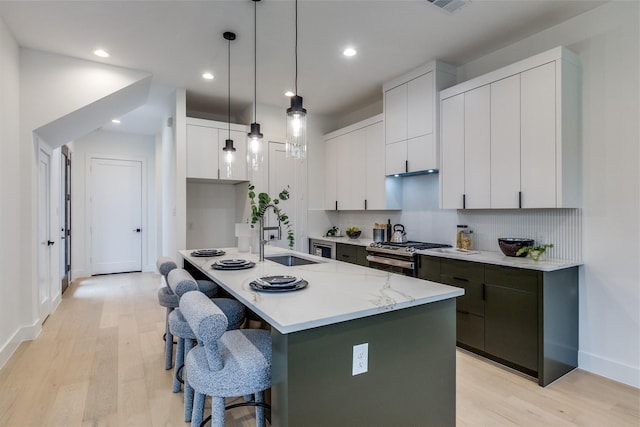 417 Wayne St, Dallas, TX 75223 - kitchen featuring stainless steel gas range oven, a kitchen bar, light wood finished floors, a sink, and a center island with sink