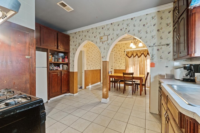 kitchen with light tile patterned flooring, sink, white refrigerator, ornamental molding, and black gas range