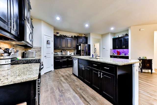 kitchen featuring light stone countertops, appliances with stainless steel finishes, a kitchen island with sink, and sink