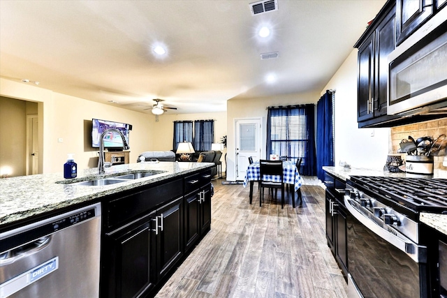 kitchen with appliances with stainless steel finishes, sink, ceiling fan, light hardwood / wood-style floors, and light stone countertops