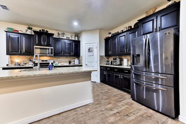 kitchen featuring sink, backsplash, stainless steel appliances, light stone countertops, and light wood-type flooring