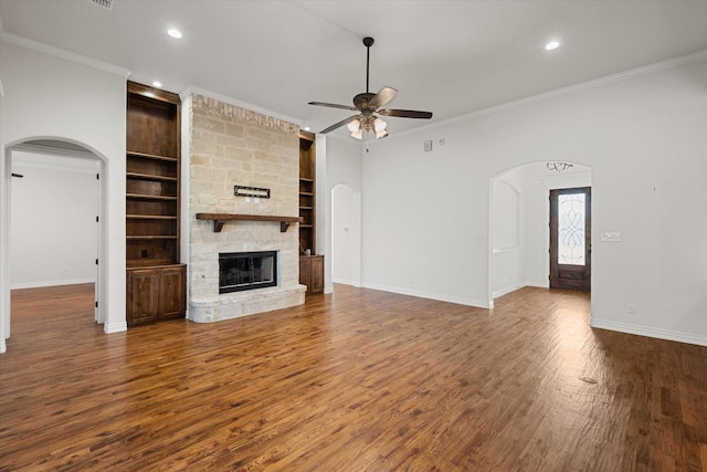 unfurnished living room with ceiling fan, ornamental molding, built in shelves, dark hardwood / wood-style flooring, and a stone fireplace